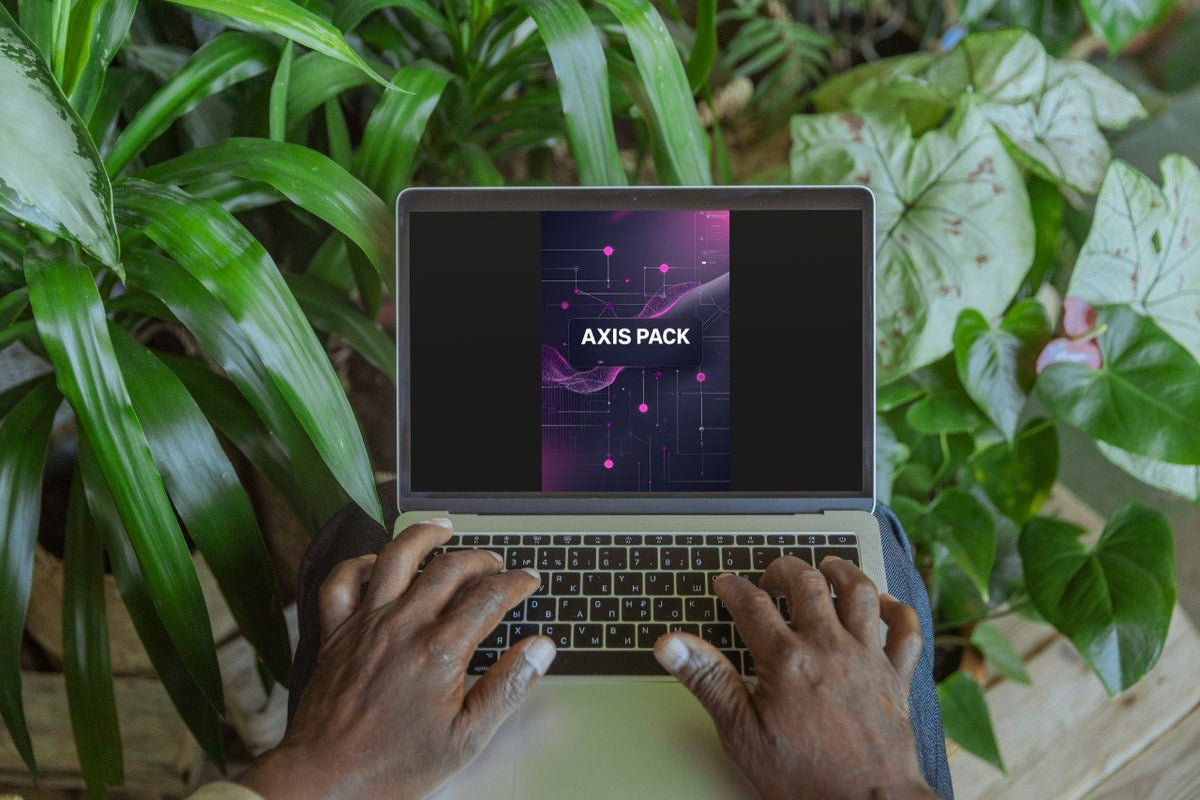 A top-down view of a person typing on a laptop surrounded by lush green houseplants. The laptop screen displays a digital graphic template titled 'AXIS PACK' with a dark purple and pink abstract design.